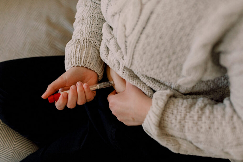 A woman injects herself in the abdomen with an injection pen