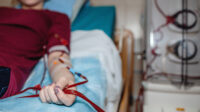 Woman in red top lies on hospital bed receiving dialysis from a machine on right