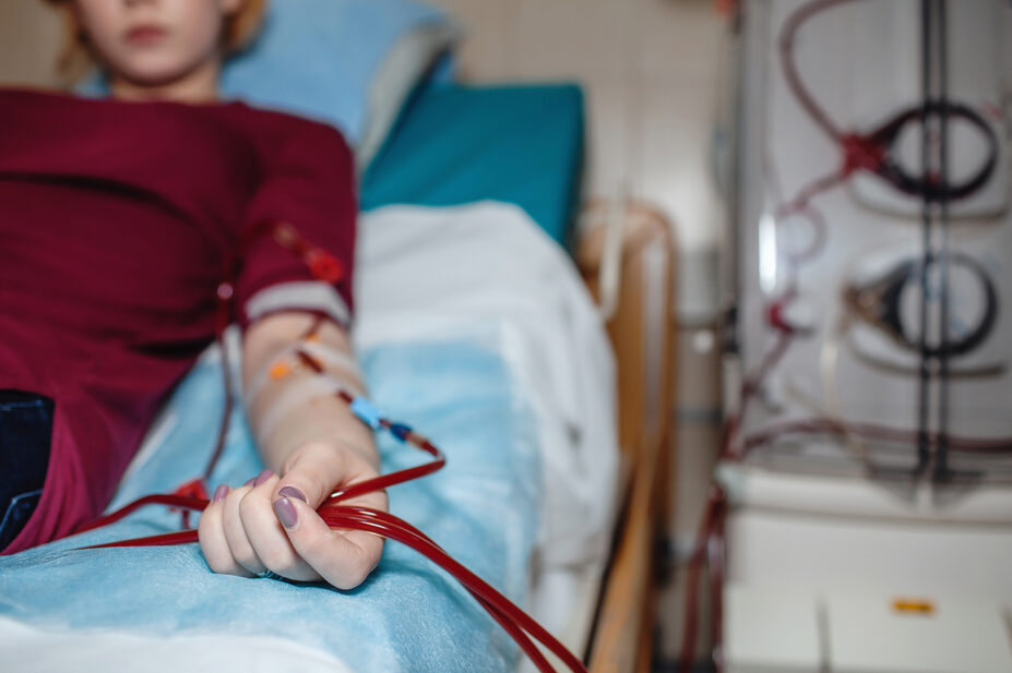 Woman in red top lies on hospital bed receiving dialysis from a machine on right