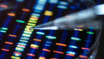 Genomic Research, Scientist holding a DNA sample in a vial with the profile results on screen in the lab