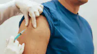 An older man receives a vaccine in his upper arm