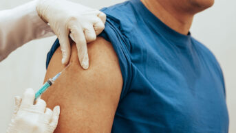 An older man receives a vaccine in his upper arm