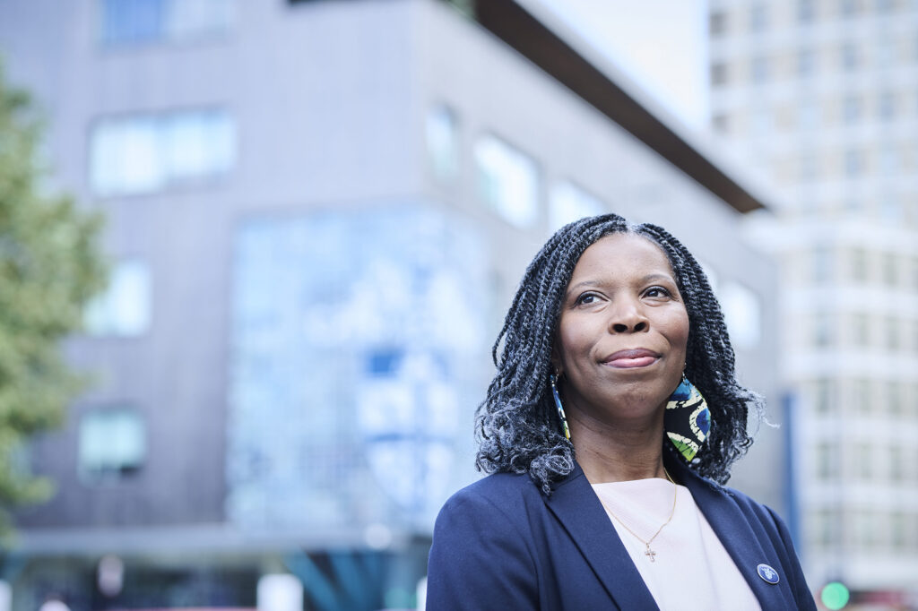 Tase looks serious wearing a dark blazer and behind her the RCPharm building and crest is visible