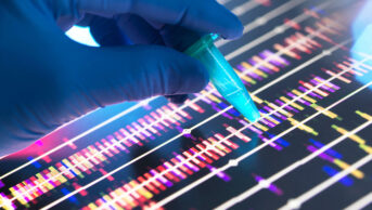 Genomic Research, Scientist holding a DNA sample in a vial with the profile results on screen in the lab