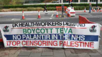 A UK health worker solidarity banner calling for a boycott of Teva Pharmaceuticals, to get Palantir out of the NHS and to stop censoring Palestine, positioned putside the encampment facing the US Embassy in Nine Elms, London. The Community Camp for Palestine marks two years of continuous presence at its encampment site. Protesters attend rallies and demonstrations calling for Palestinian rights and an end to the war in Gaza.