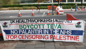 A UK health worker solidarity banner calling for a boycott of Teva Pharmaceuticals, to get Palantir out of the NHS and to stop censoring Palestine, positioned putside the encampment facing the US Embassy in Nine Elms, London. The Community Camp for Palestine marks two years of continuous presence at its encampment site. Protesters attend rallies and demonstrations calling for Palestinian rights and an end to the war in Gaza.